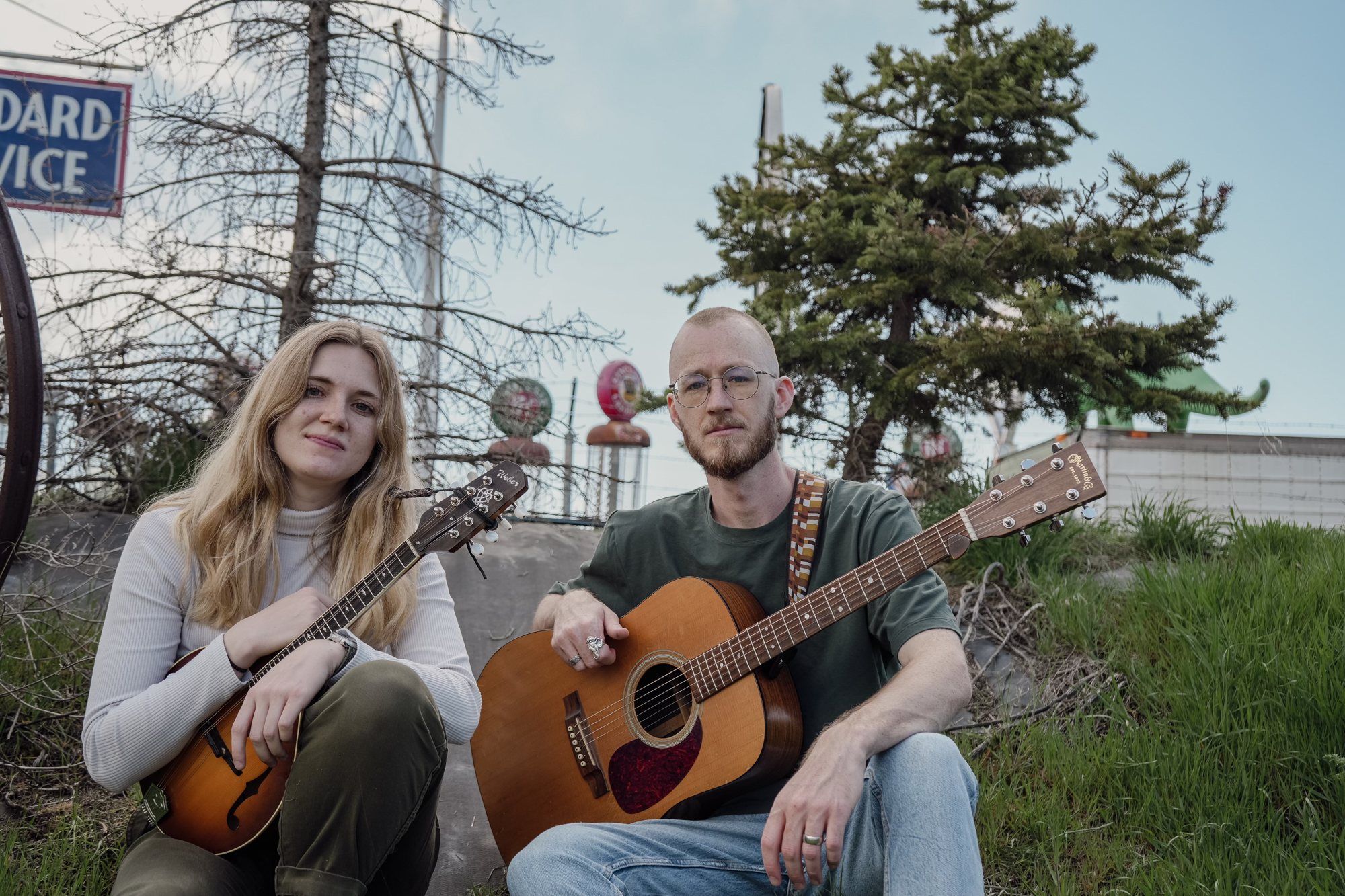 Brielle and Isaac sitting in the grass with a mandolin and a guitar